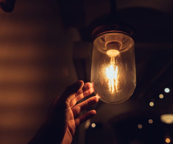 Hand reaching for a vintage light bulb. Dark and abstract concepts