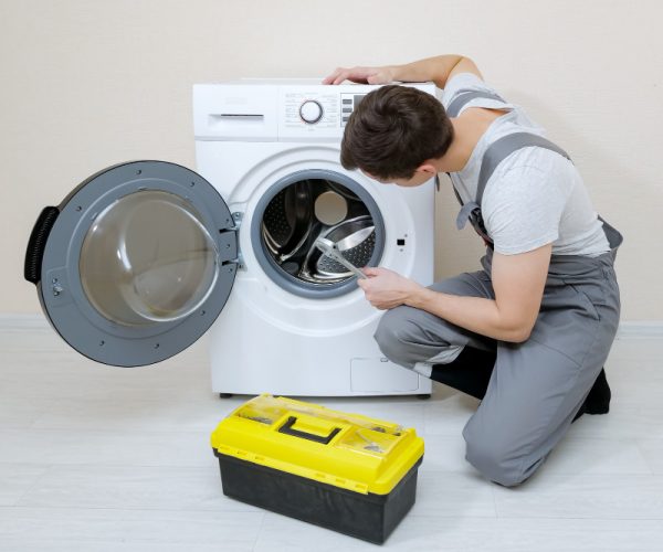 serviceman-repairs-broken-washing-machine-near-beige-wall